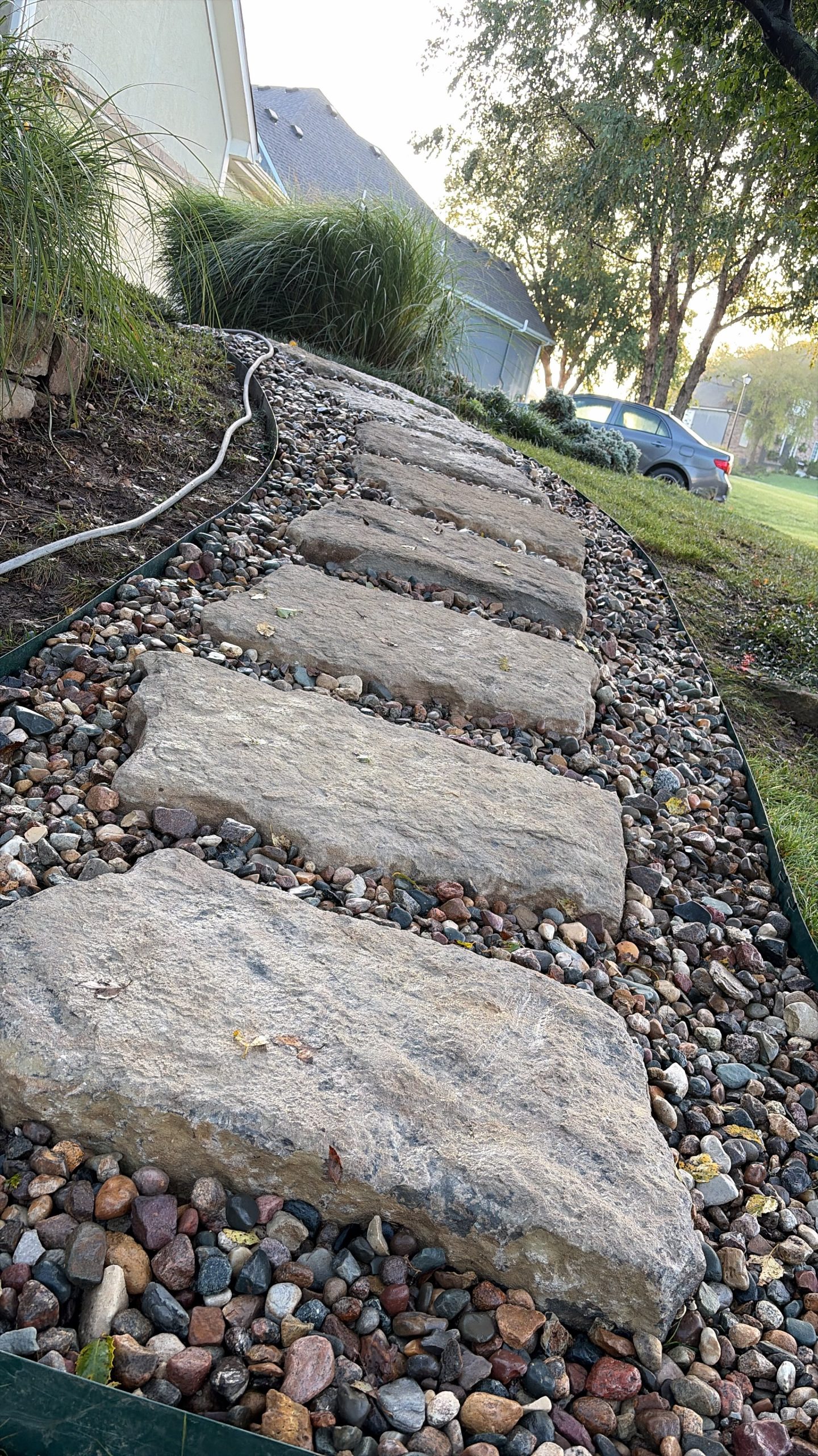 Rock drainage channel installed around mature trees on a sloped Grandview property